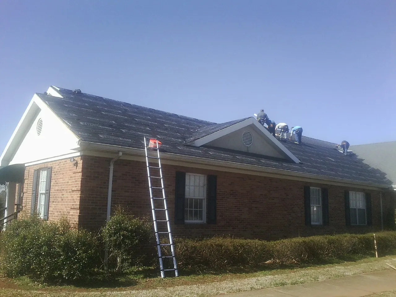 Crew tearing shingles off a brick ranch roof with a ladder set — Metal Roof Repair work by our crew in Riggins