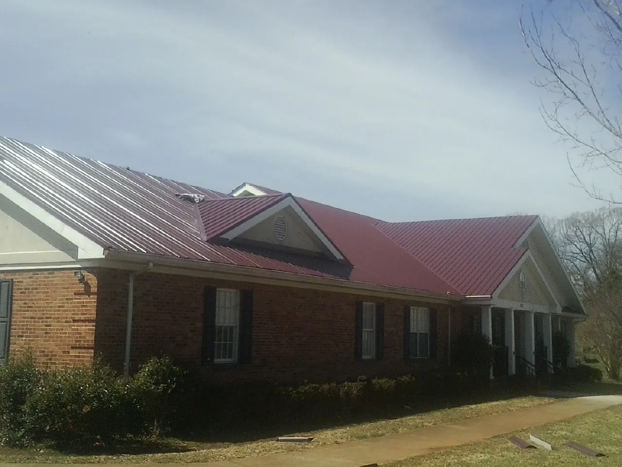 Red metal roof with gabled entries on a long brick building, from a Hail Damage Roof Repair job in Riggins