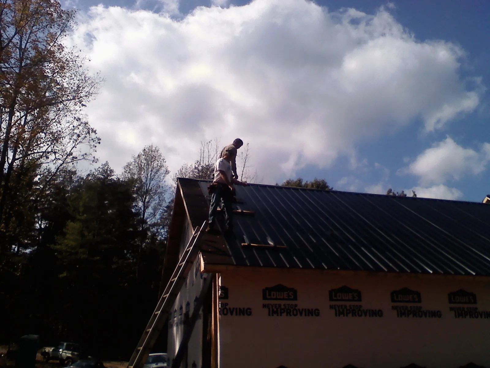 Roofer fastening dark metal panels high against a cloudy sky, from a Roof Inspection job in Riggins